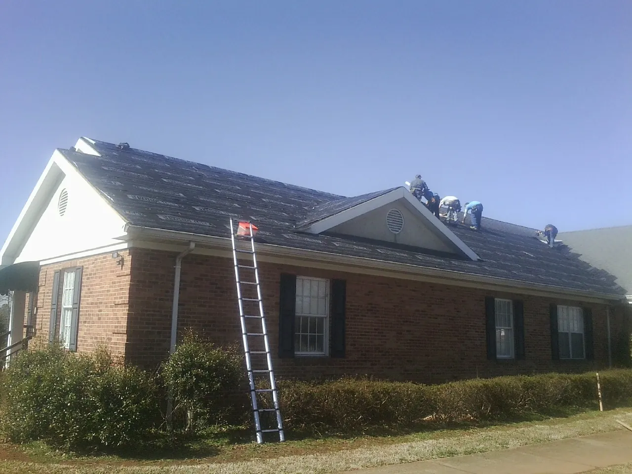 Crew tearing shingles off a brick ranch roof with a ladder set — Emergency Roof Repair work by our crew in Marlton
