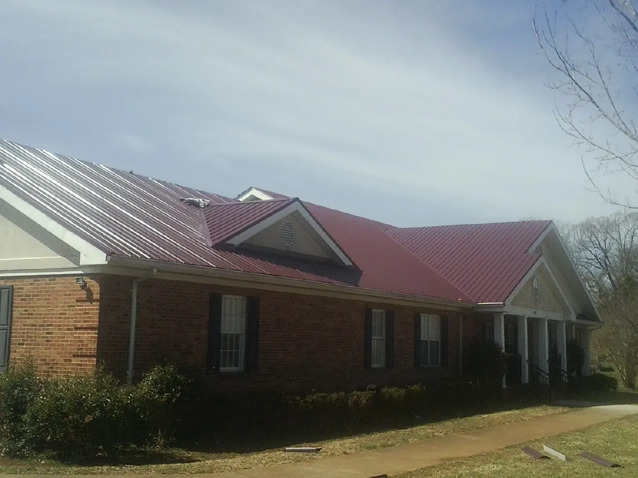 Red metal roof with gabled entries on a long brick building, from a Hail Damage Roof Repair job in Marlton