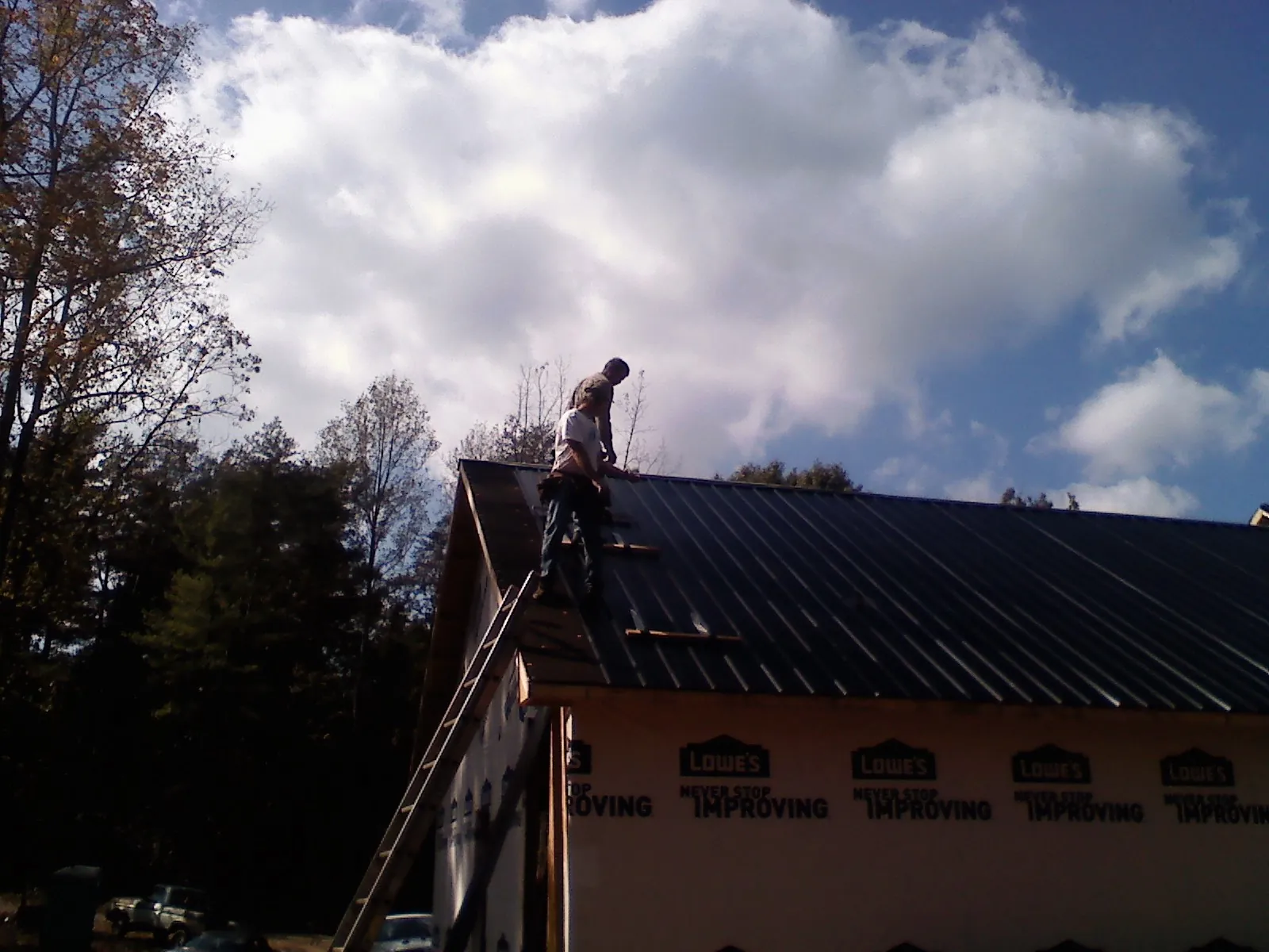 Roofer fastening dark metal panels high against a cloudy sky, from a Roof Inspection job in Marlton