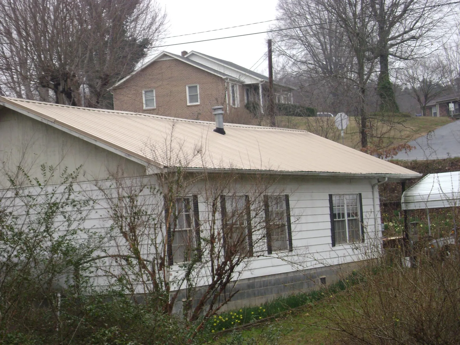 Tan metal roof on a white sided house set into a hillside — Commercial Roofing by Roofing Brothers in Marlton